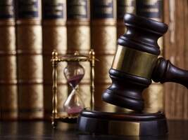 Gavel at the downward point of contact with hourglass and books in the background