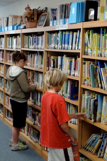 Kids in Library looking at books on the shelf
