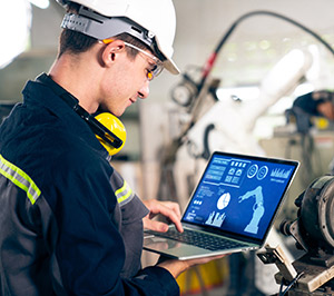 Image showing an engineer wearing safety equipment and looking at a laptop interface